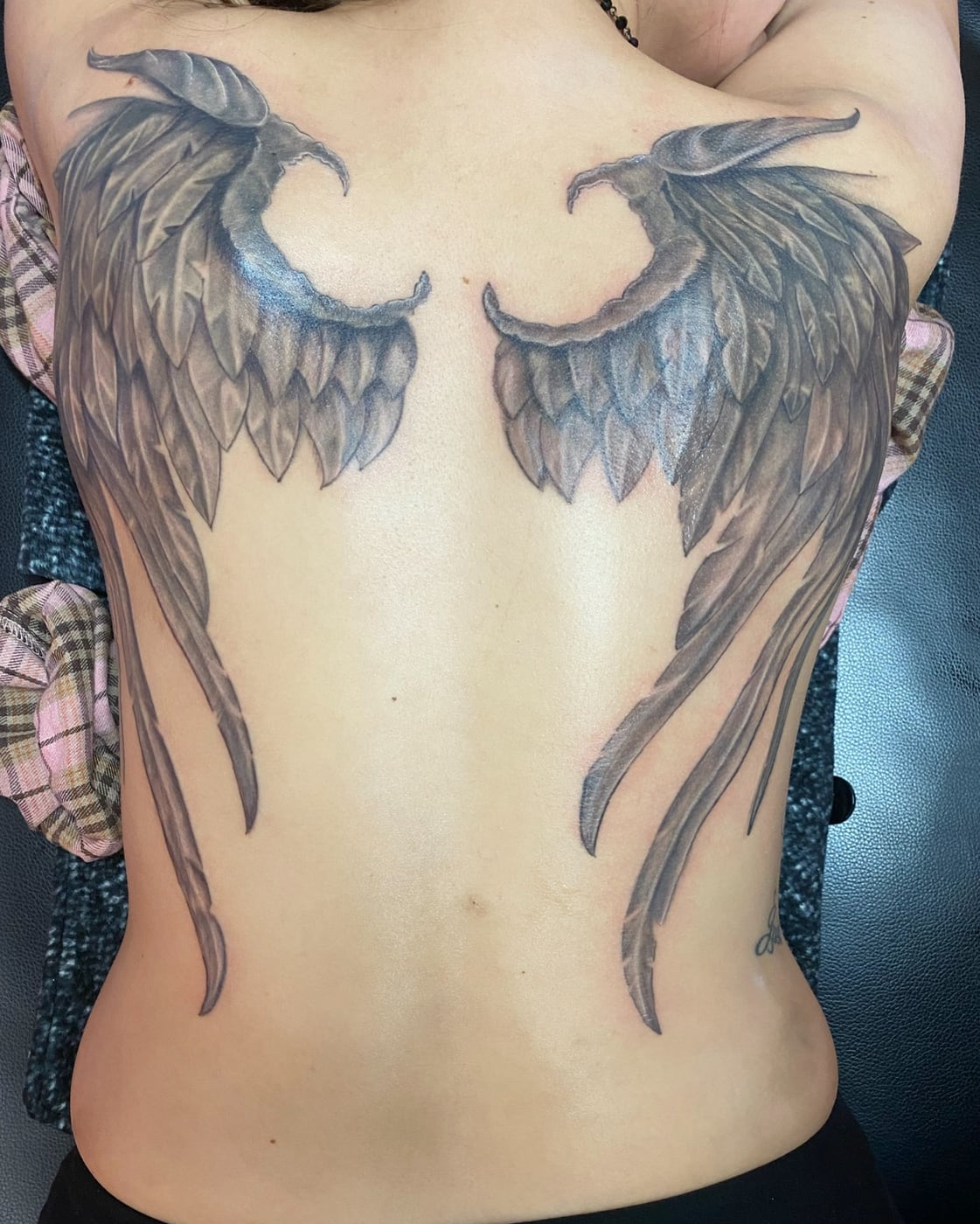 Large black and grey angel wings spanning a full back, individually rendered feathers tapering down to the waist