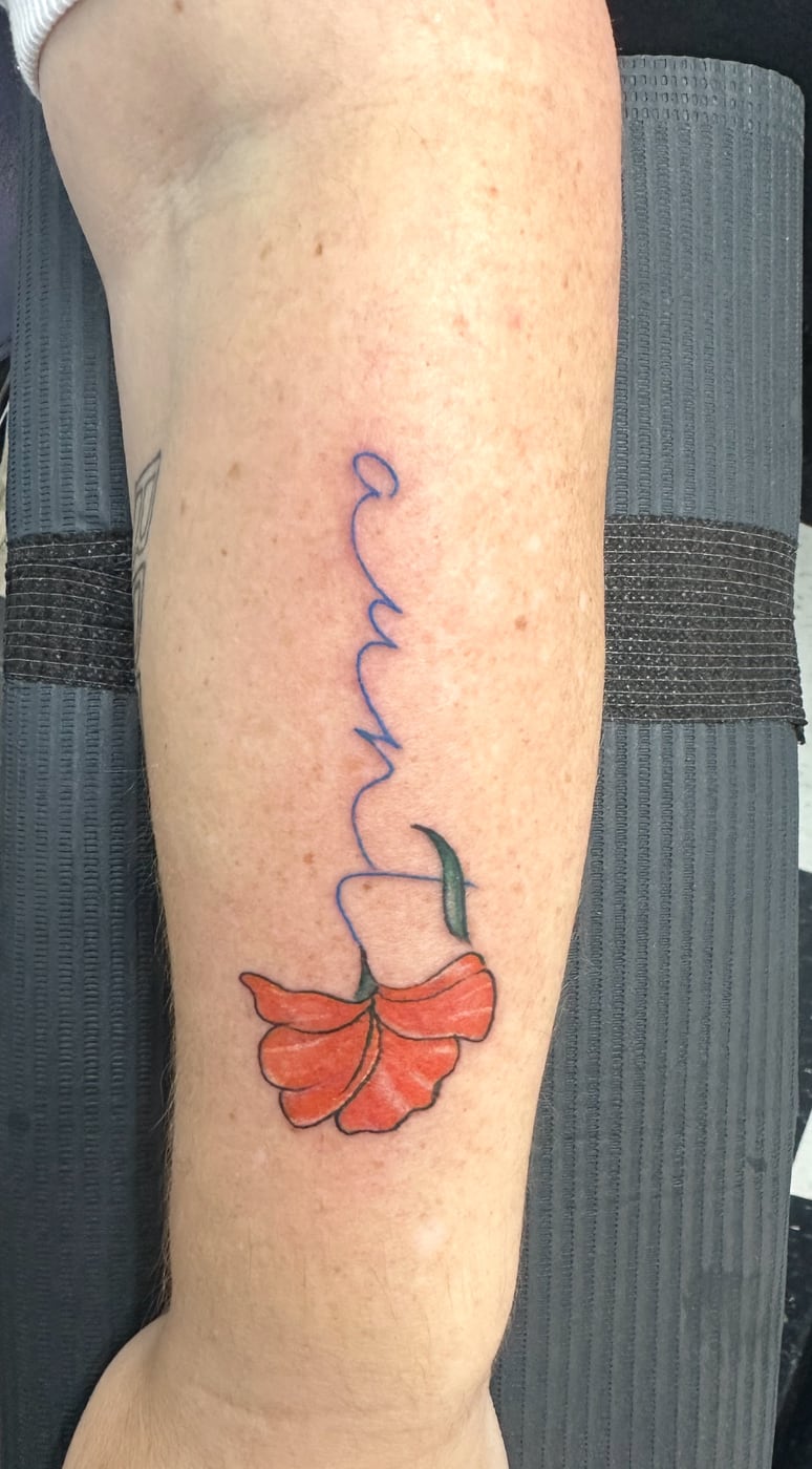 Delicate single-needle script running down the inside of a forearm, finished with a small red-orange poppy