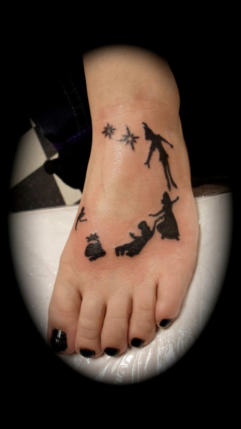 Fine line foot tattoo of small storybook silhouettes and a trail of stars curving around the side of the foot