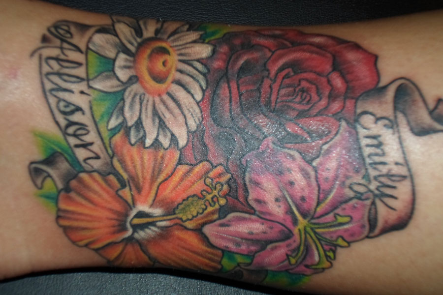 Full-color forearm tattoo of a daisy, red rose, orange hibiscus and pink stargazer lily with two name banners scrolling through them