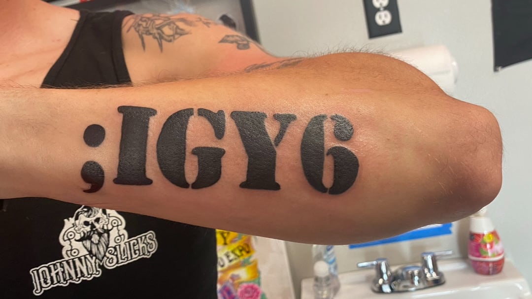 Bold black block lettering reading a semicolon followed by I G Y 6 across the outside of a forearm