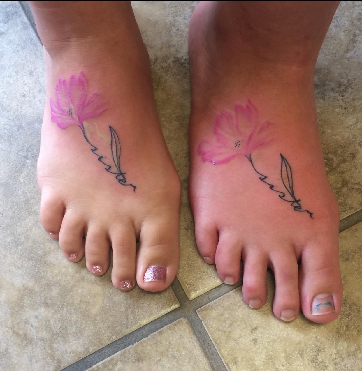 A matching pair of fine line foot tattoos, each a pink blossom on a stem with a word in fine script alongside it