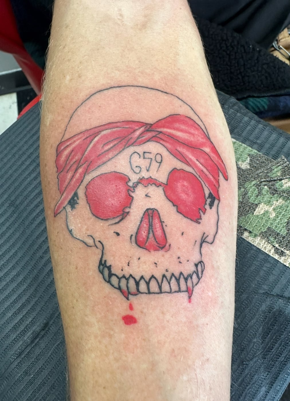 Color forearm tattoo of a skull wearing a red bandana, with red sockets and a drop of blood below the jaw