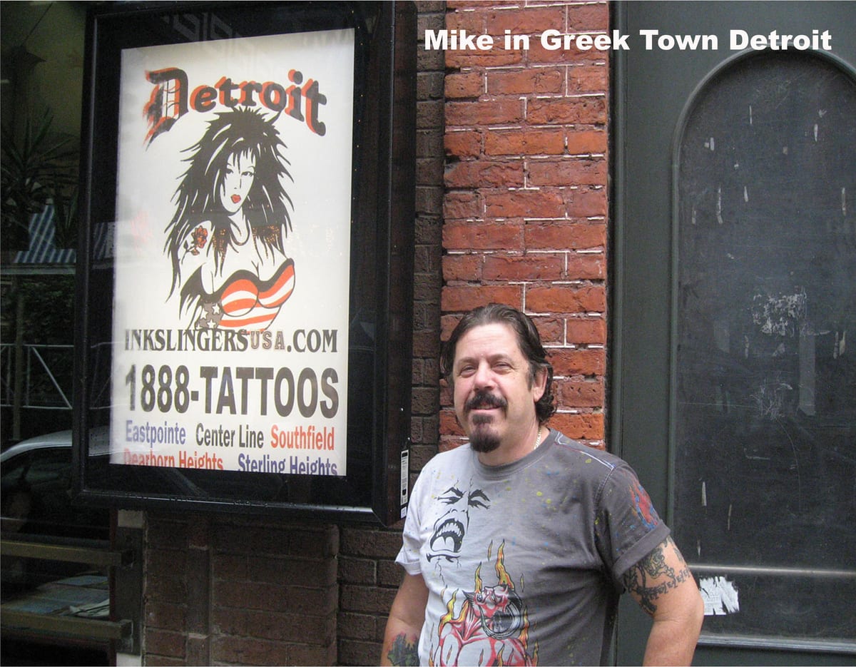 Mike Jeziak standing beside an illuminated Inkslingers sign on a brick wall in Greektown, Detroit
