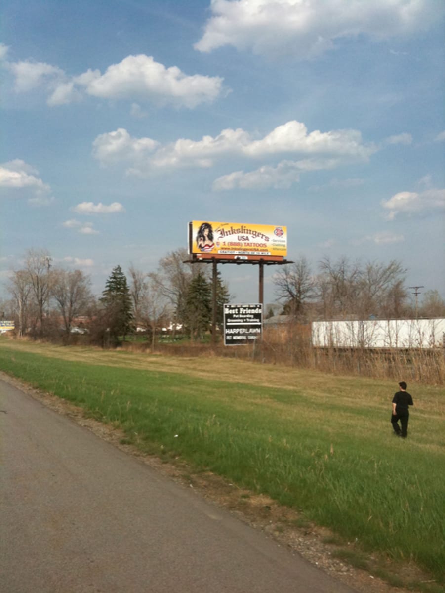 Roadside billboard advertising Inkslingers USA with a freephone tattoo number, standing in a field beside a road