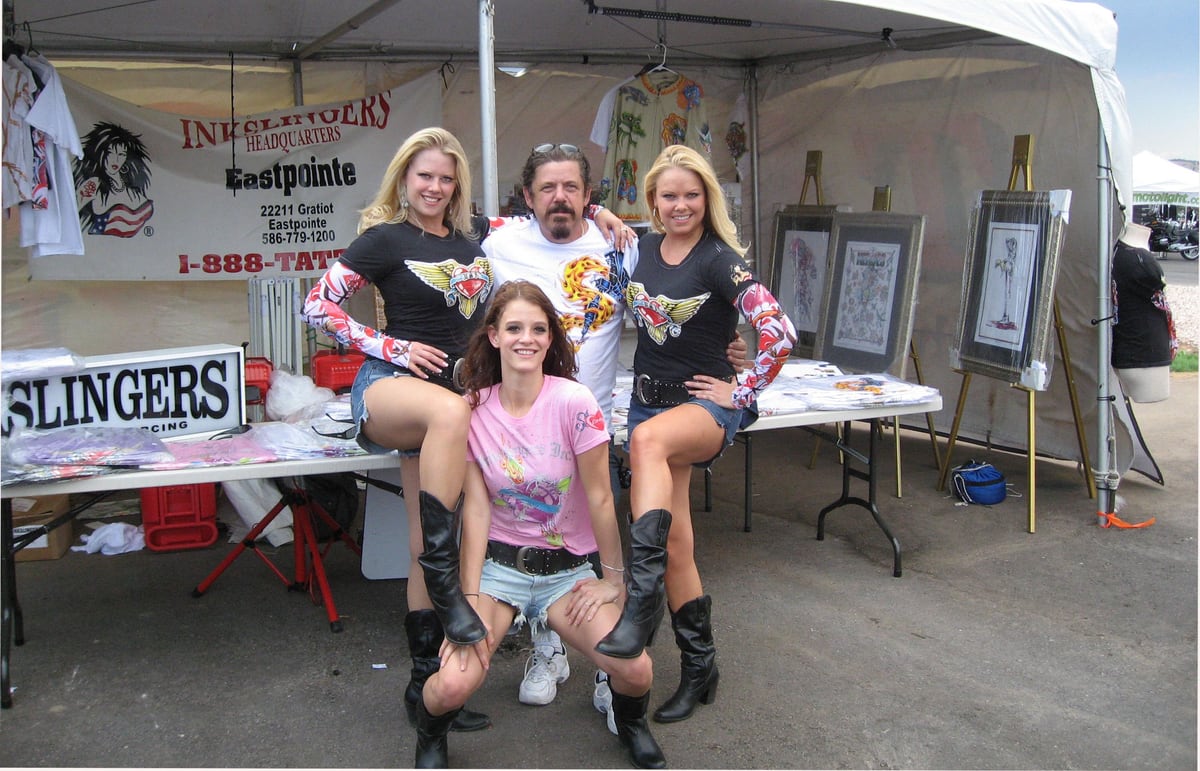Inkslingers trade stand under a marquee at the Sturgis rally in 2006, staff and models in front of banners and artwork